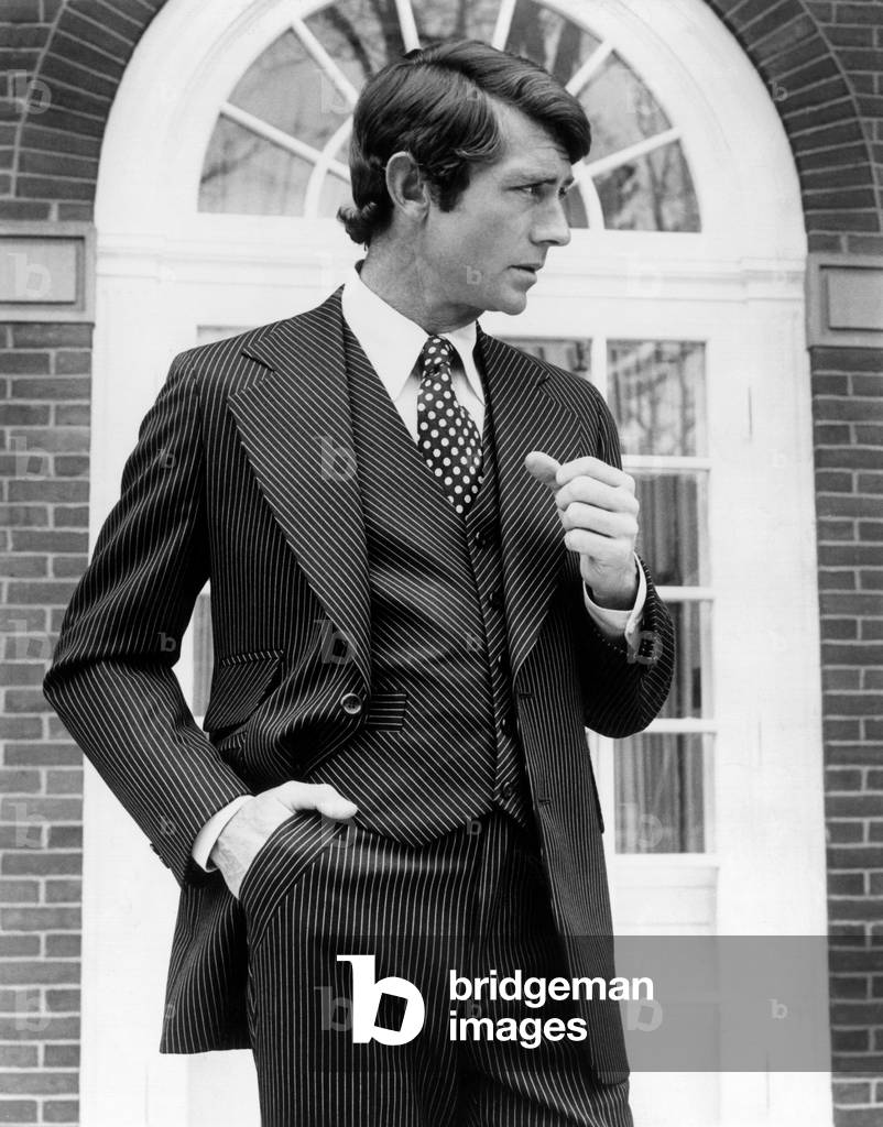 Brown wool and silk three-piece suit is pin striped with gold and white. It has angled stripes on the vest, pockets and lapels. It is worn with an ecru polyester/cotton shirt with brown, gold and white silk polka dot tie. Sept. 1974