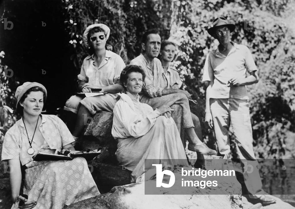 THE AFRICAN QUEEN, center front to rear: Katharine Hepburn, Humphrey Bogart, Lauren Bacaal, director John Huston (right) on location on set, 1951