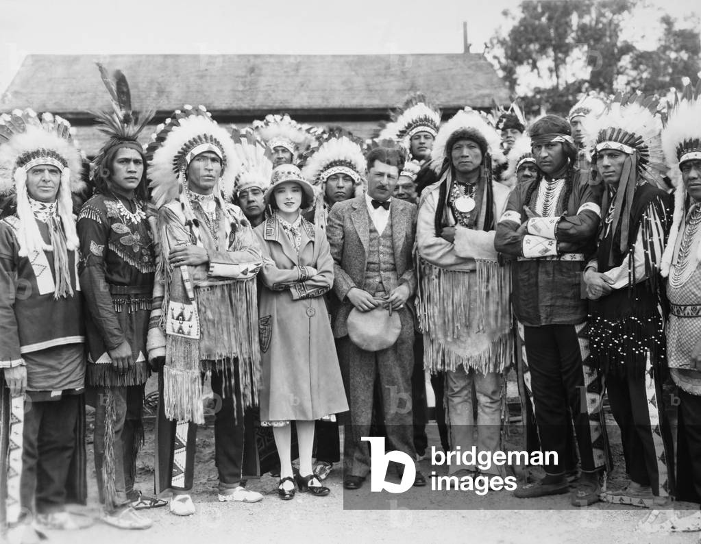 ELLA CINDERS, center from left: Colleen Moore, director Alfred E, Green with Indian tribe on location, 1926
