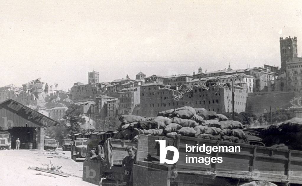 The city of Teruel, with a few destroyed buildings, after the bombings of the Spanish civil war. In the foreground the backs of two trucks, one empty and the other full of bags. Further off a garage, other trucks and a few soldiers can be seen, 08/1938 (b/w photo)