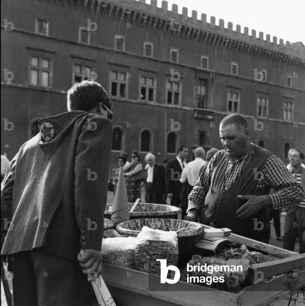 Vendor of peanuts, tree nuts and olives in Piazza Venezia in Rome during the funeral of Palmiro Togliatti August 25, 1964 (b/w photo)