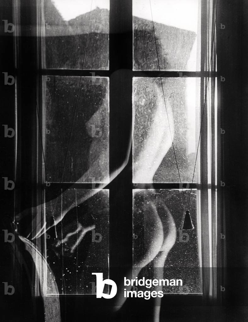 Female nude seen from behind; a chair nearby with a window in the forefront