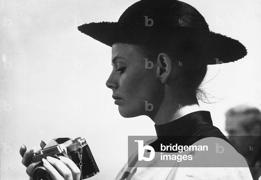 Portrait of Britt Ekland in cleric's dress while adjusting a camera.