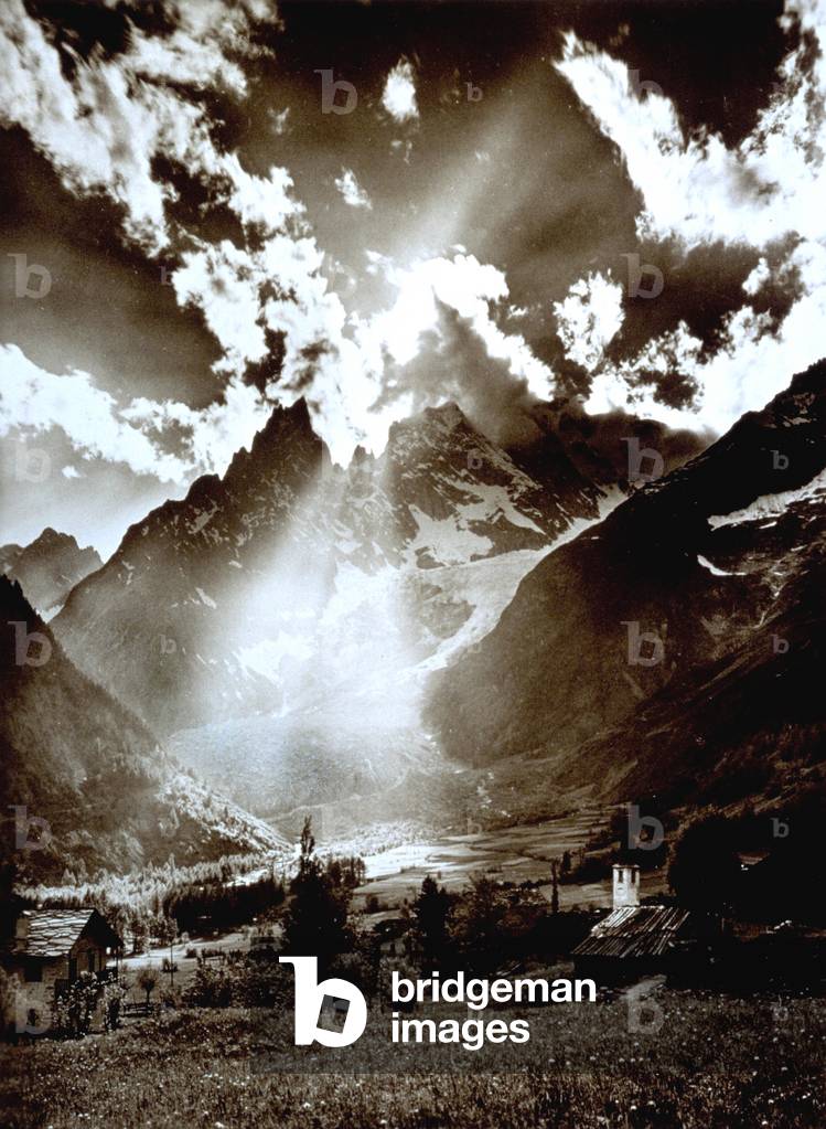 View of Val Veny with Mont Blanc in the background. In the foreground, a few houses from the town of Entrèves. The peaks which remain uncovered by clouds are, from the left, Aiguille Noire, La Dame Englaise, Pic Gugliermina, and Aiguille Blanche