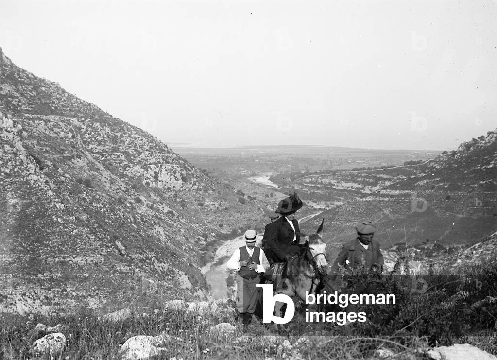 A woman on horseback with two men in the countryside, Cassibile