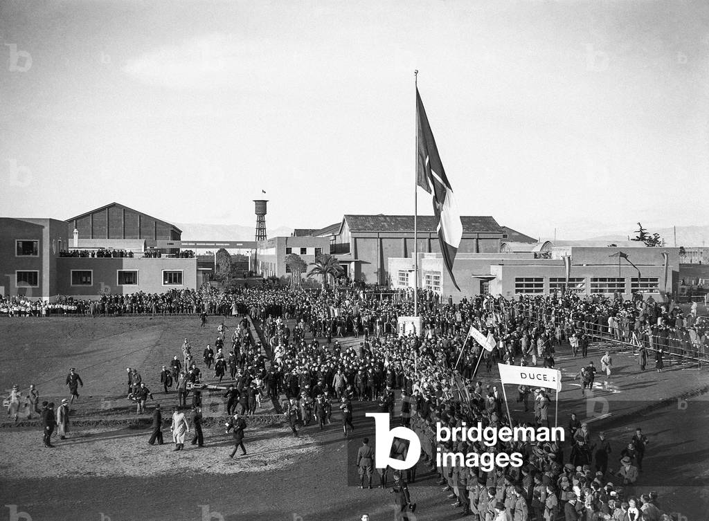 Spectators and fascist militiamen attend, along the avenue of Cinecittà in Rome, the passage of Benito Mussolini and the authorities during the inauguration ceremony, 28/04/1937 (b/w photo)