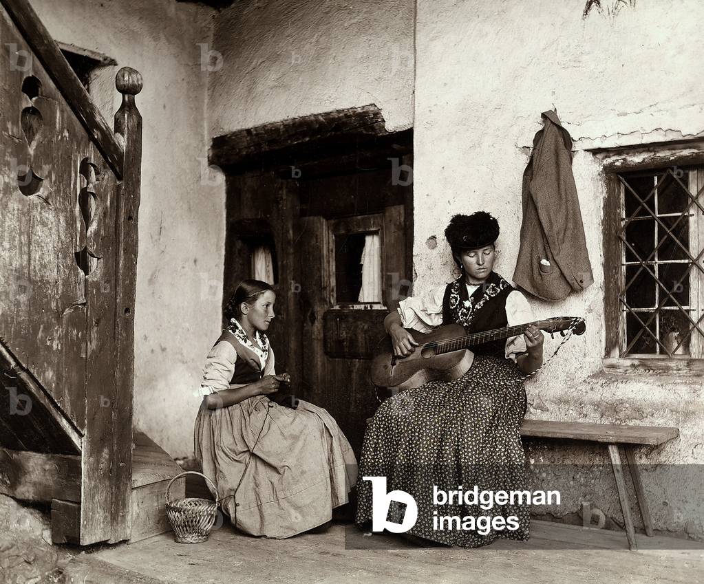 Woman playing the guitar next to a young girl crocheting, Casa Apollonio Cortina