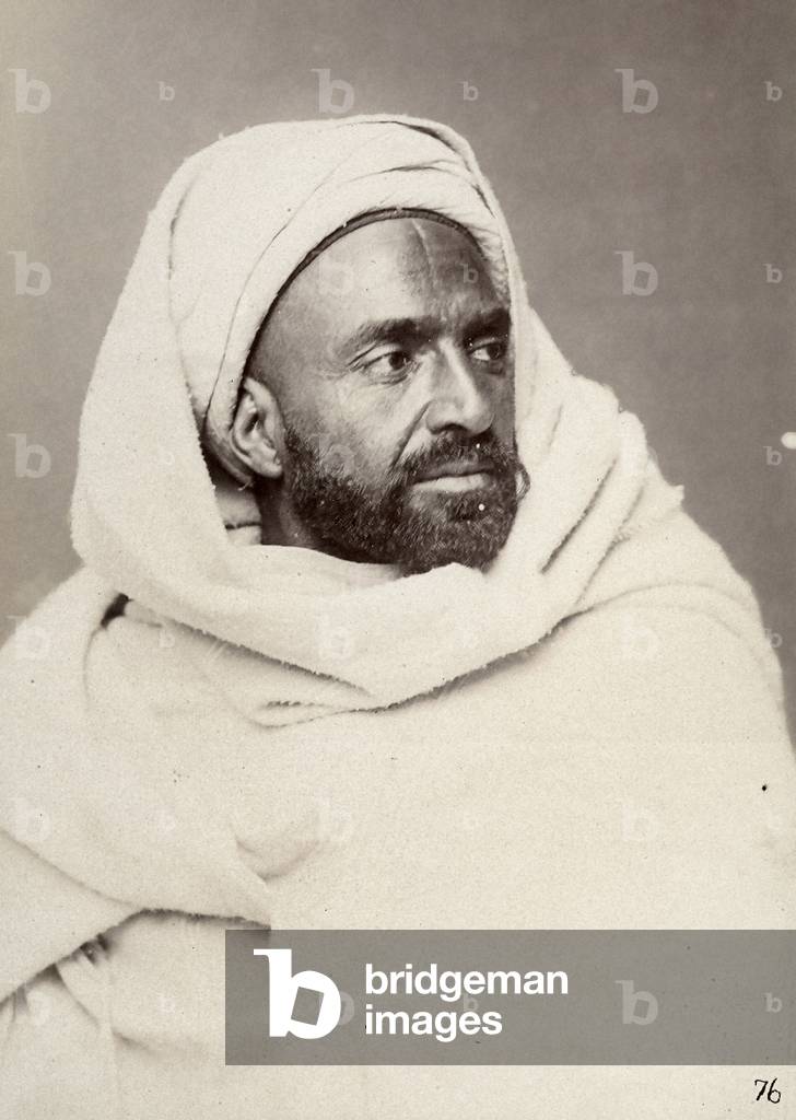 The image portrays a young Tunisian bearded man, wrapped up in a mantle,  1870 (print on double-weight paper)