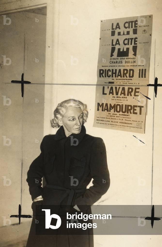Portrait of the actress Berthe Bovy in front of a publicity poster of the Theatre La Citè.