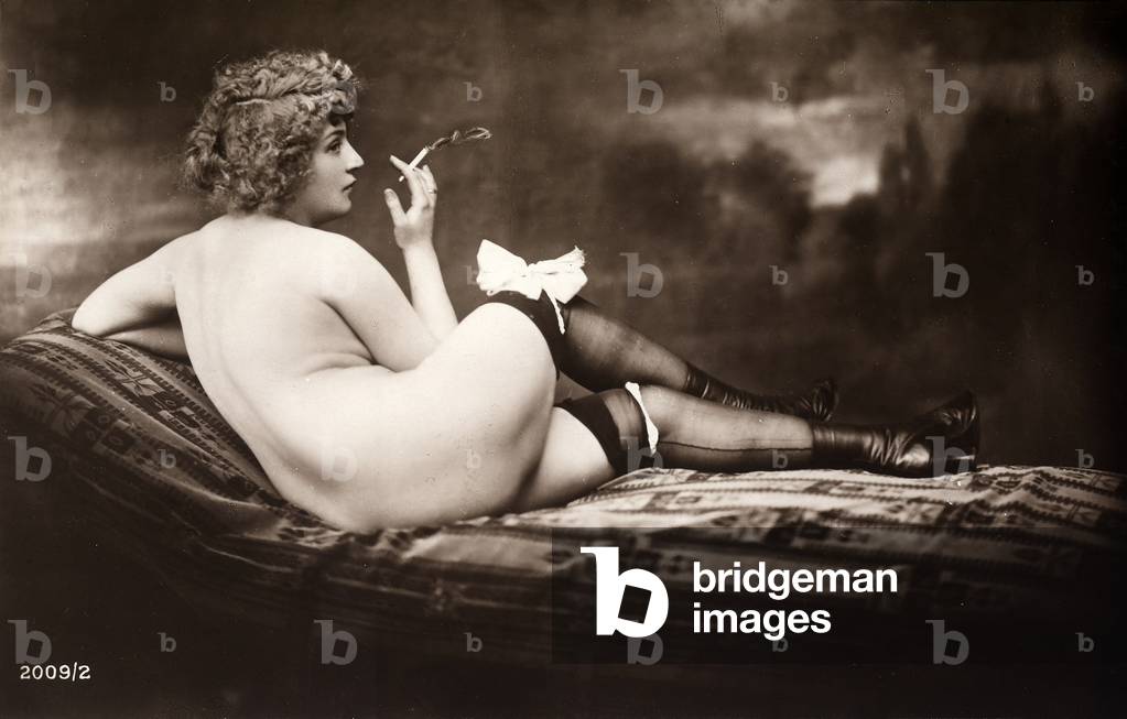 Portrait of a young woman posing naked, with her back turned, as she smokes a cigarette