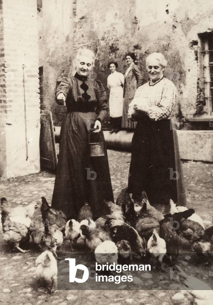 Two elderly women feed their chickens. (b/w photo)