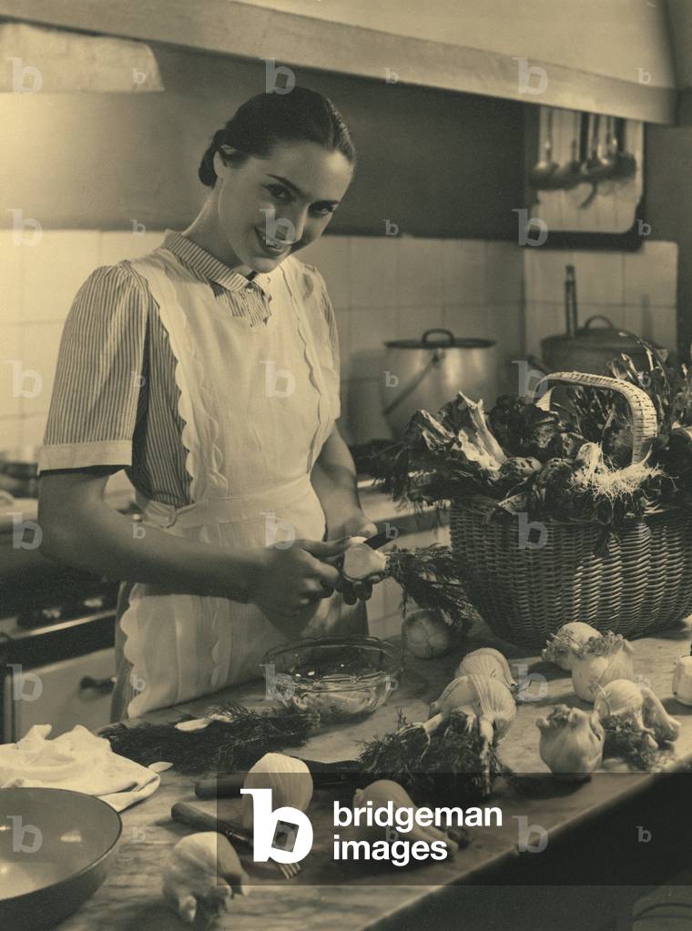 Young woman with apron in the kitchen in front of a table with vegetables