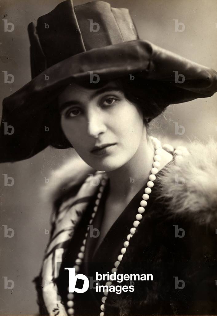 Half-bust portrait of alda Borelli, wearing a wide-brimmed hat, a fur coat and a long string of pearls