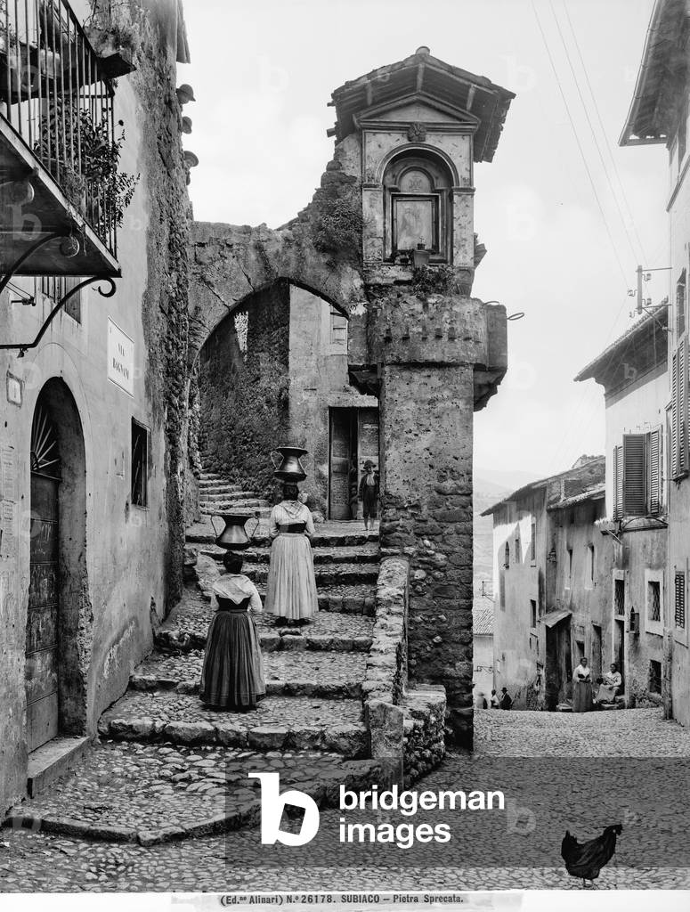 Characteristic street in the town of Subiaco. In the foreground are two women carrying water pitchers on their heads and a rooster