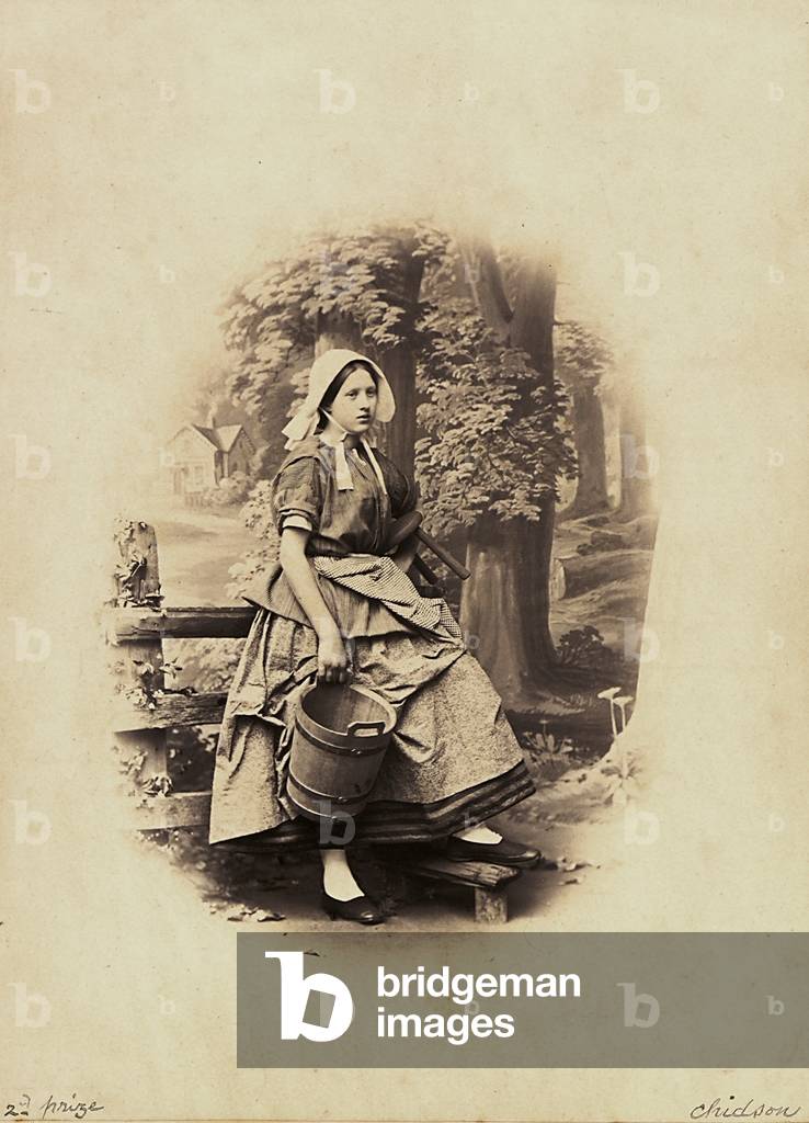 A woman in farmers dress with a bucket for milking, portrayed in a photographic studio Great Britain