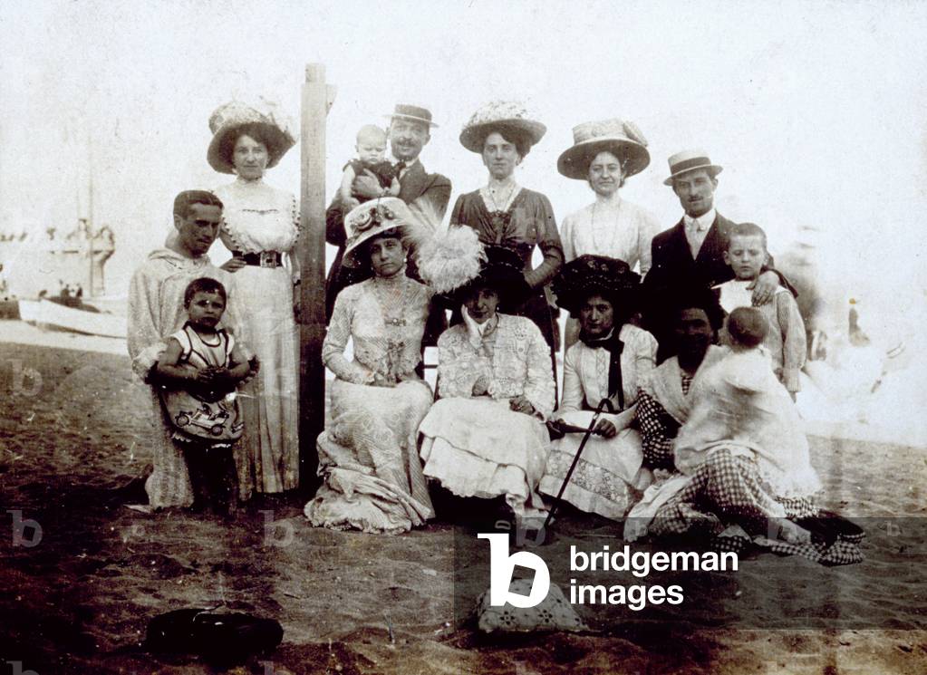 Group of persons in elegant day dress shown on a beach in Savona