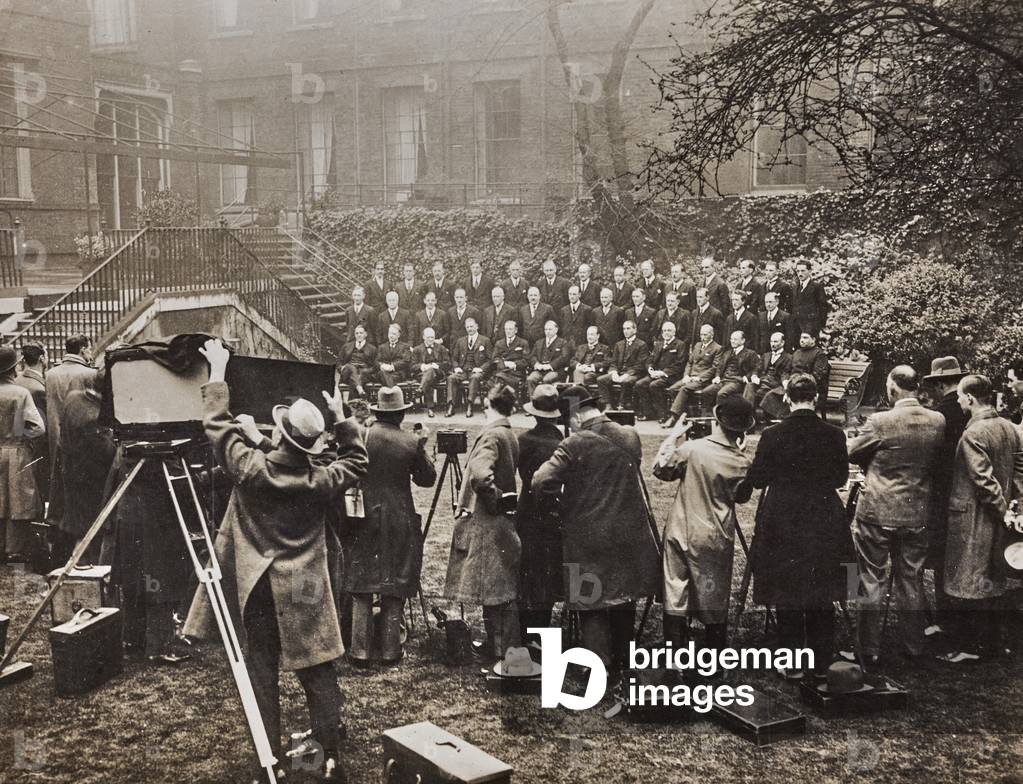 Some photographers taking pictures of the members of the Imperial Conference, standing in three rows in a garden in London.