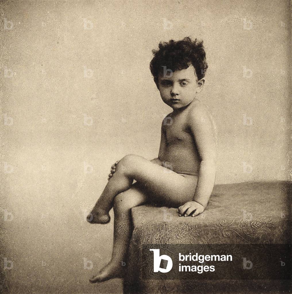Portrait of a seated nude child, posing with his legs crossed
