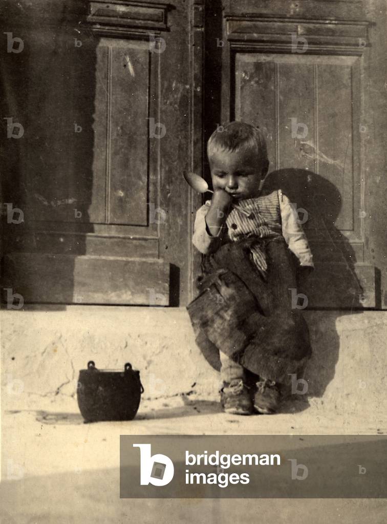 A little boy seated at the door of a house, 1910-1915 (print on double-weight paper)