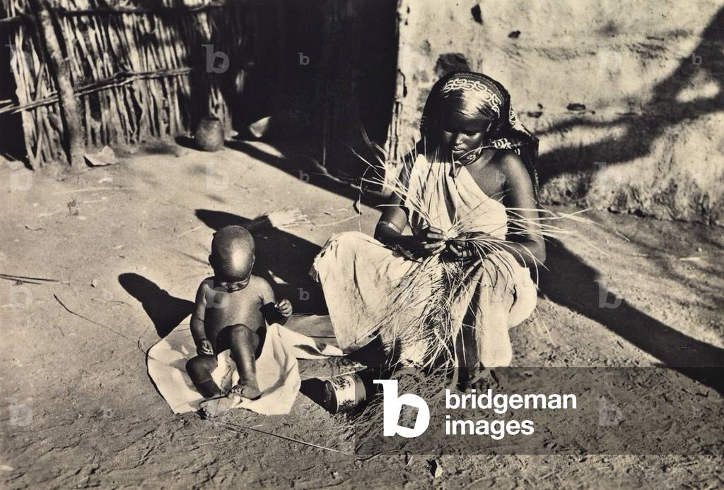 Young Ethiopian woman weaving straw next to her child, 1935 (print on double-weight paper)