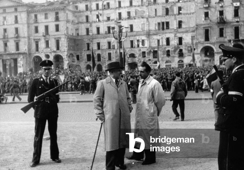 Snapshot of the official ceremony in Turin during the celebrations for the liberation of the city. In the foreground, two authoritative figures are conversing surrounded by armed carabinieri. Troops of partisans crowd Piazza Vittorio Veneto, 06/05/1945 (b/w photo)