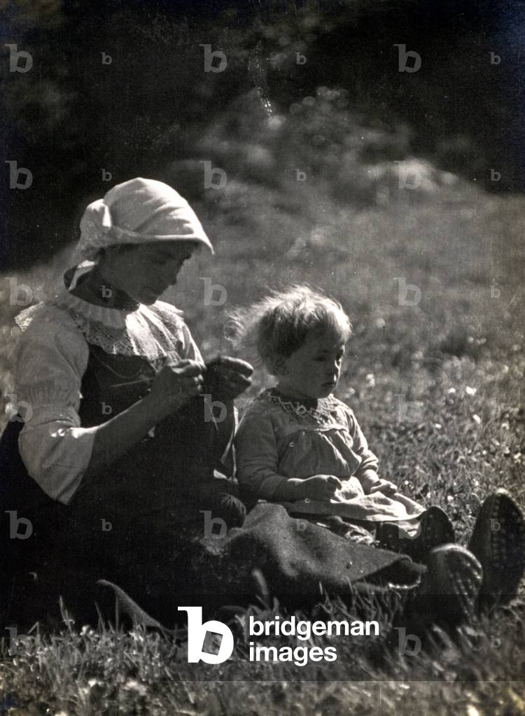 Mother and daughter sitting in a meadow. The woman is knitting