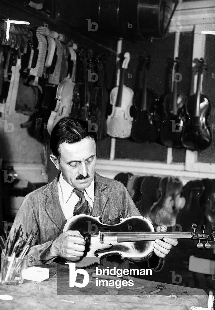 Monsieur Billotet, maker of stringed instruments, in his workshop, holding a violin.