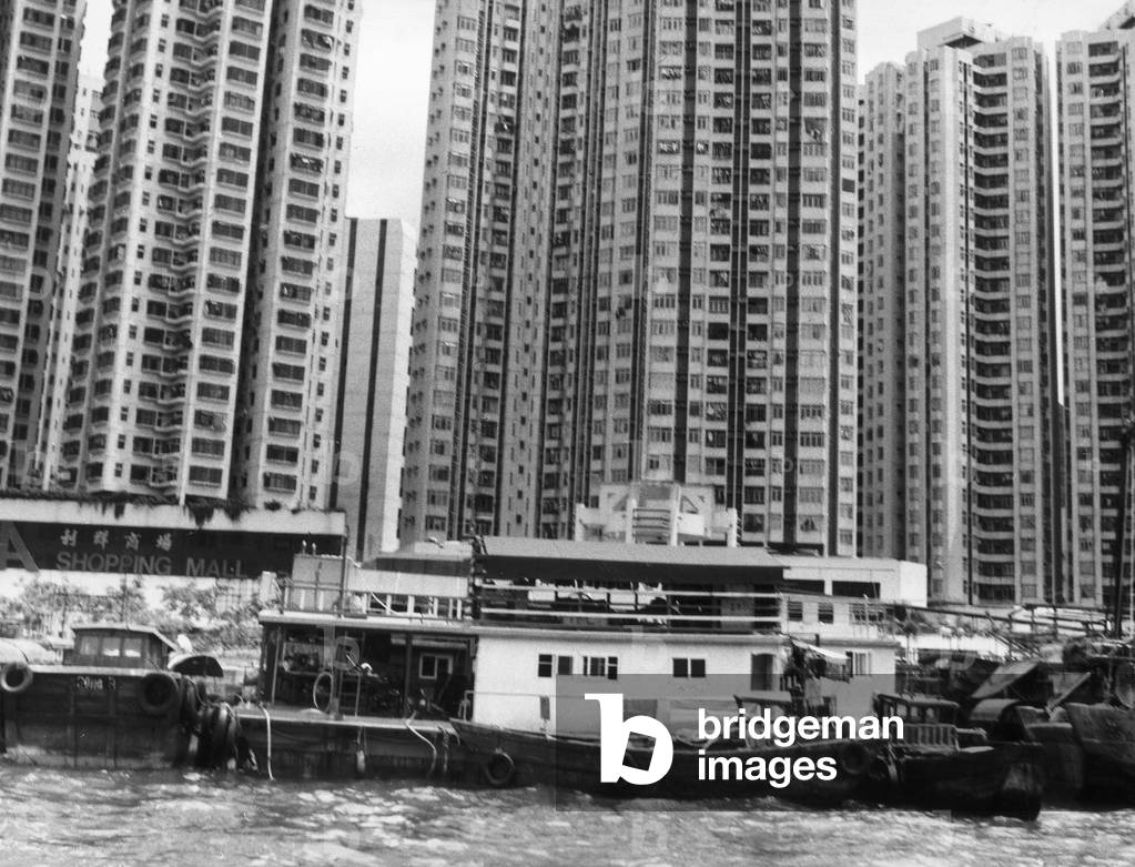 View of Hong Kong: Old boats in the foreground, against the backdrop of modern skyscrapers (b/w photo)