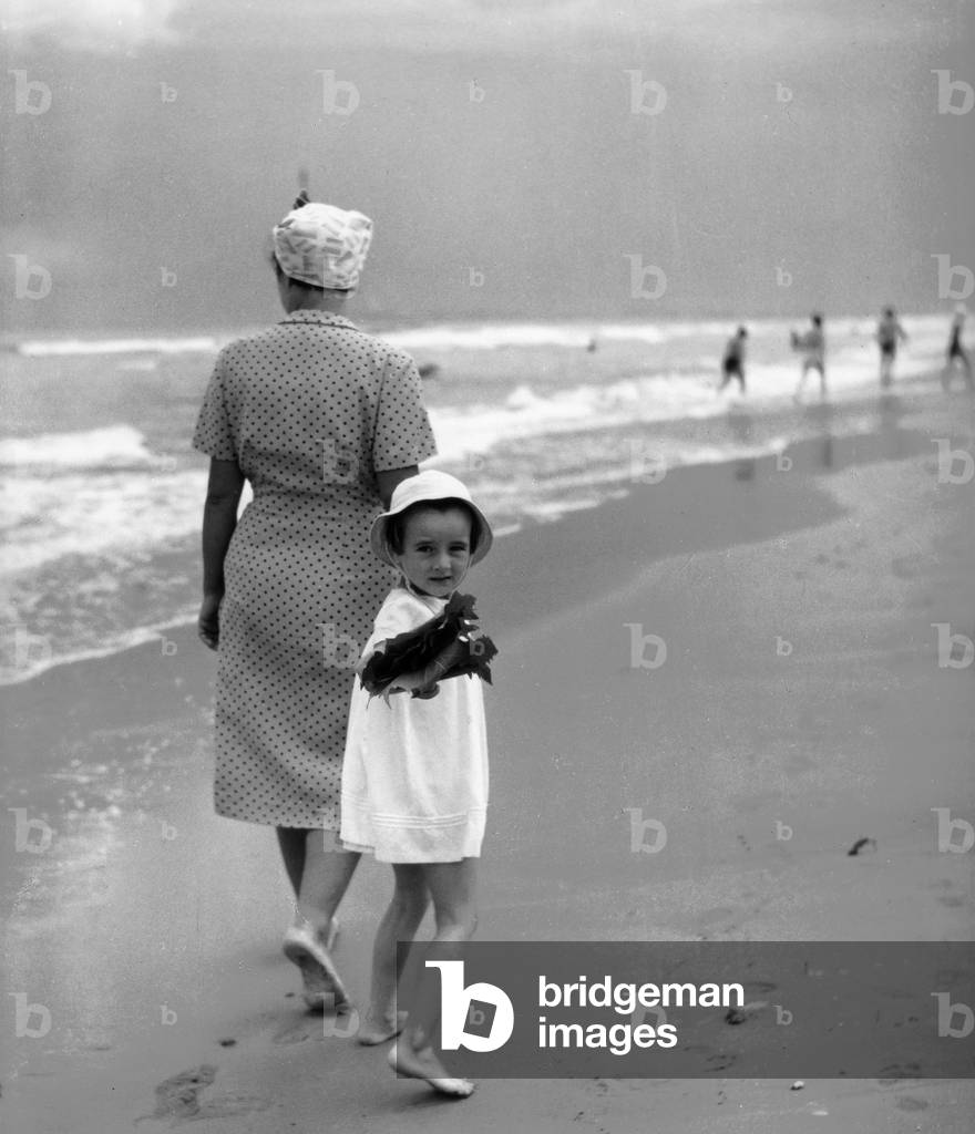 Little girl walking on the beach holding hands with mother