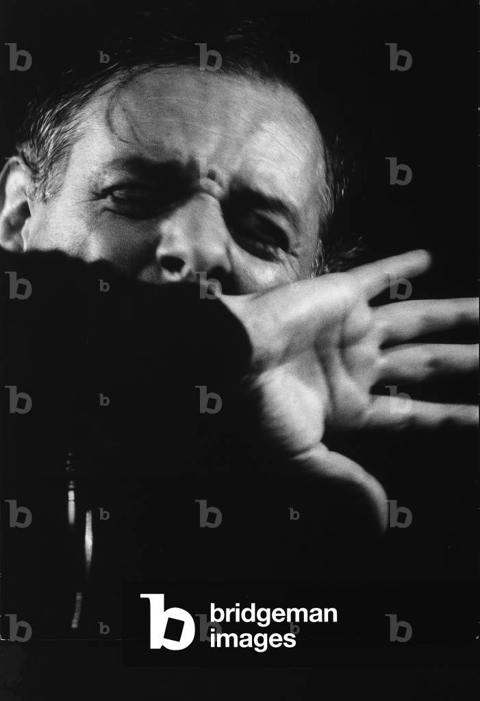 Close-up of Dario Fo while acting; the actor's eyes are closed and his hand is in front of his mouth.