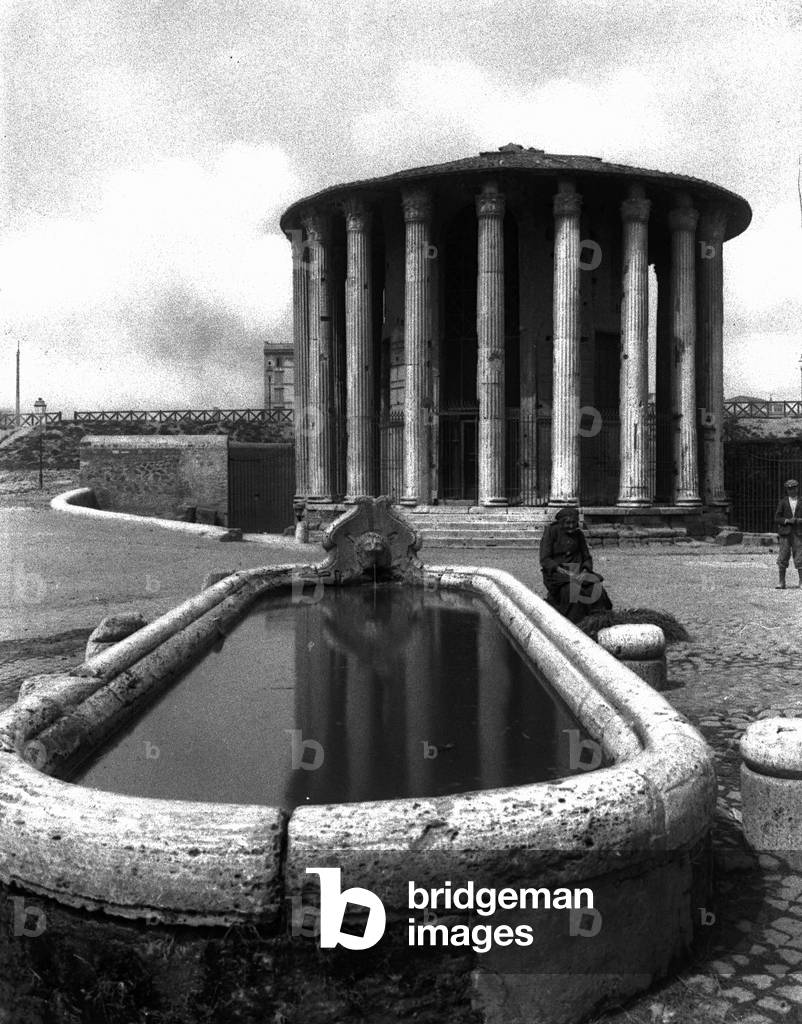 View of the Vesta Temple, in the Cattle Market, in Rome. In the foreground an old woman sitting next to a fountain can be seen