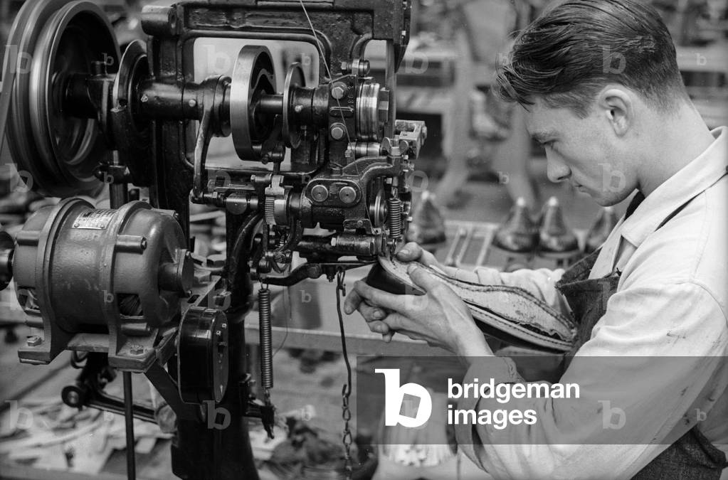 Closeup of a young worker to sew a shoe with the help of a machine inside the shoe factory Montanari