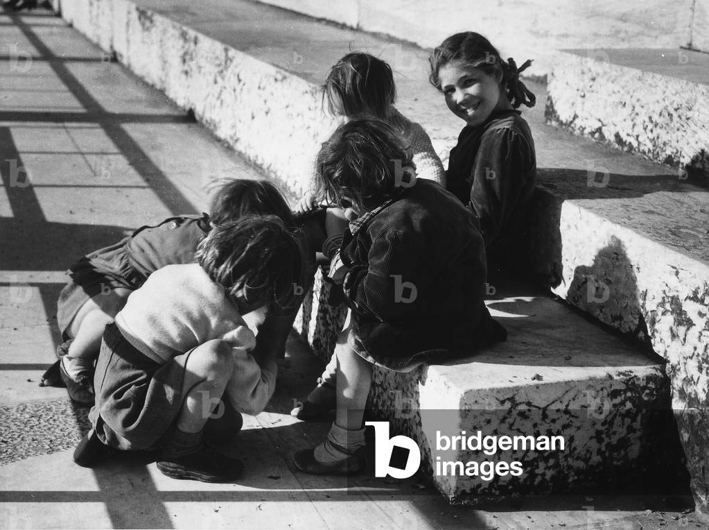 A group of children playing in the street, sitting on some steps.