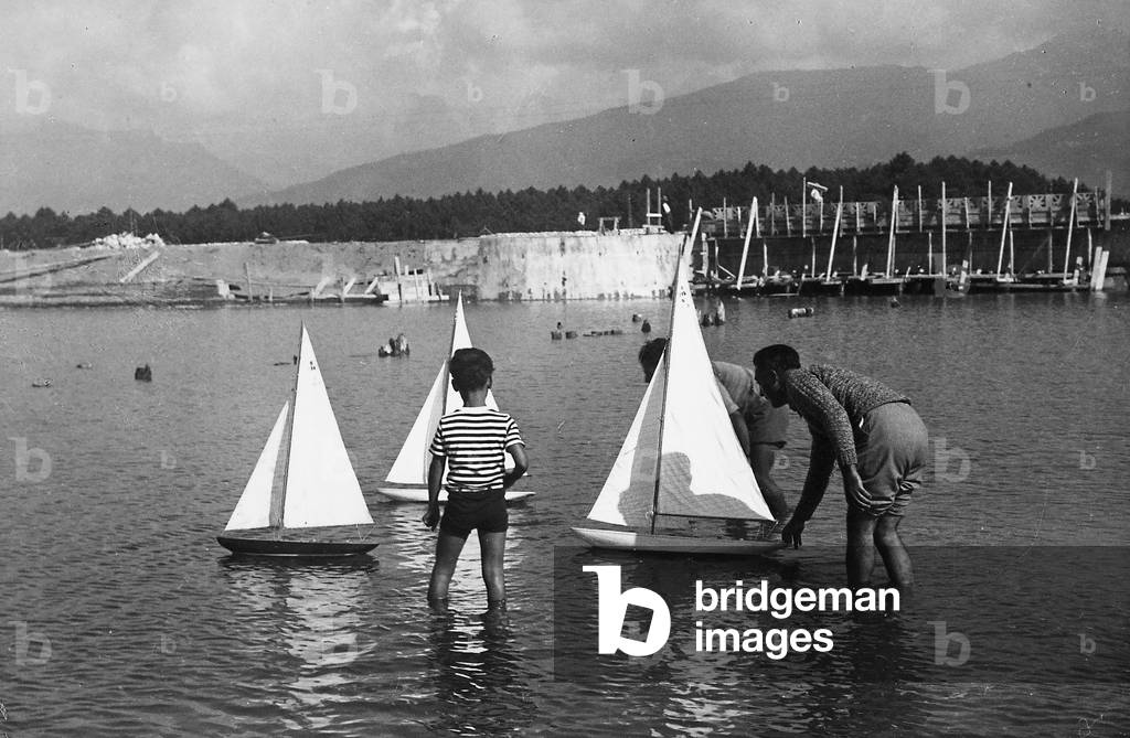 Men playing in the sea with a model boat