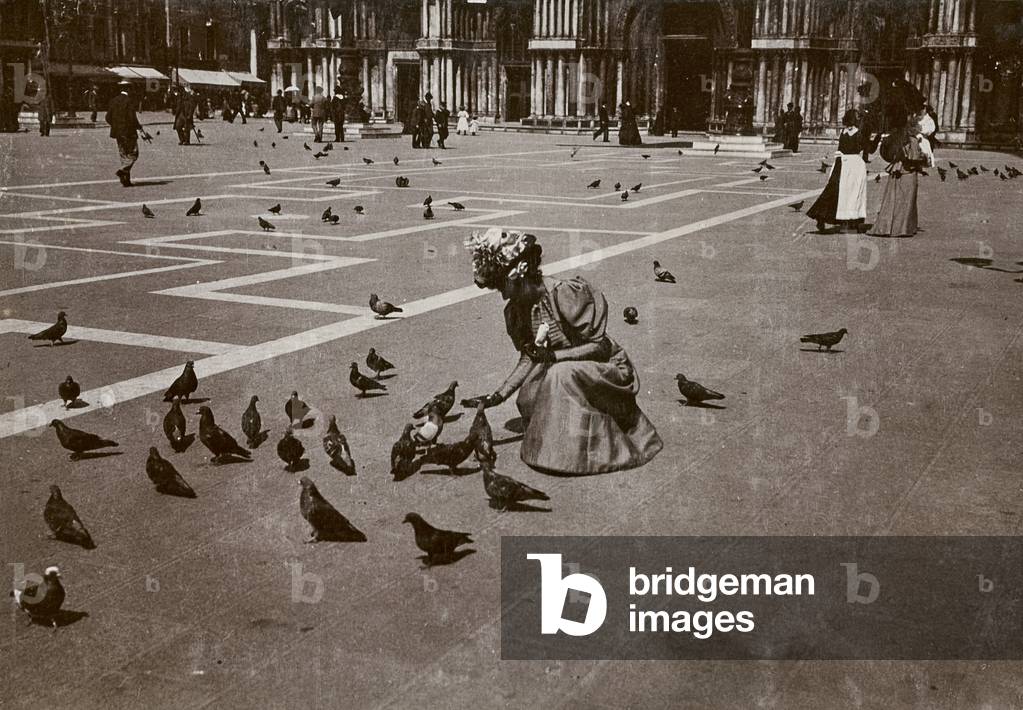 A woman bending over to feed the pigeons in Piazza San Marco, in Venice