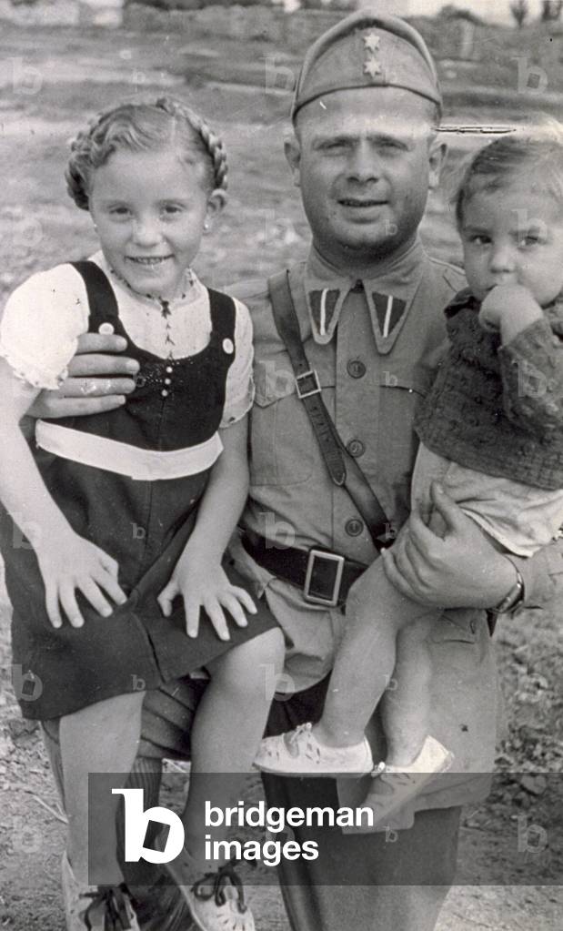 Portrait of a soldier in uniform holding two children in his arms. The little girl is smiling, while her younger brother has his hand on his mouth and looks very serious, 1938 Spain (b/w photo)