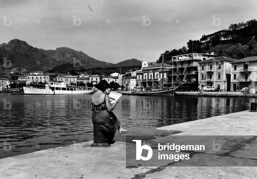 A woman reads a newspaper on the quay of the port of Porto Azzurro on Elba Island