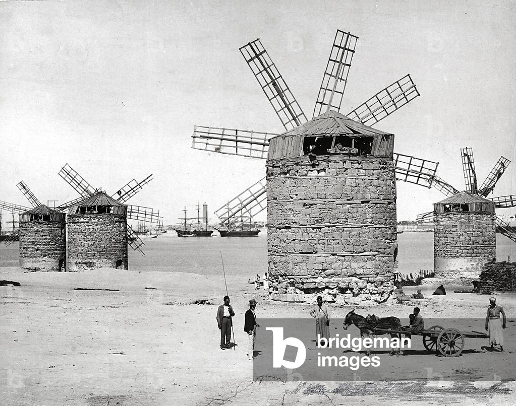Windmills on the Mediterranean Sea in Alexandria, Egypt. In front, some egyptians posing with a small cart