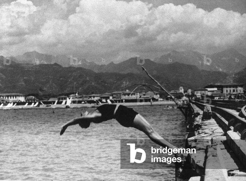 Snapshot of a young woman in a spectacular dive backwards from the jetty of Forte dei Marmi, Versilia
