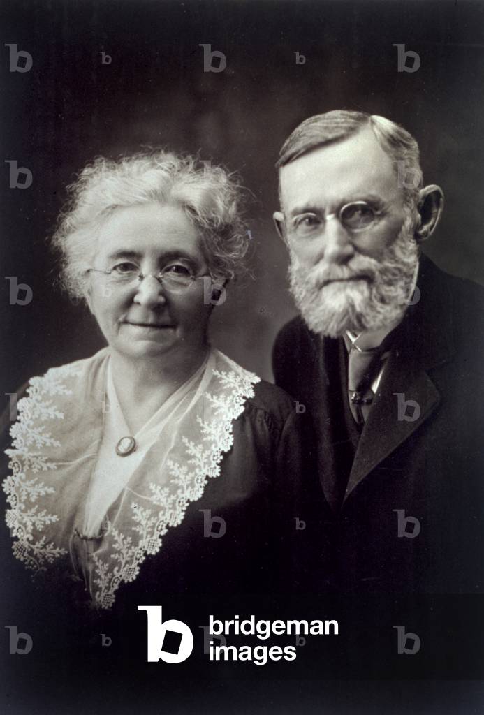 Half-length portrait of an elderly married couple. The woman is wearing a dress with a lace collar held in place by a cameo brooch, the man is wearing a dark jacket