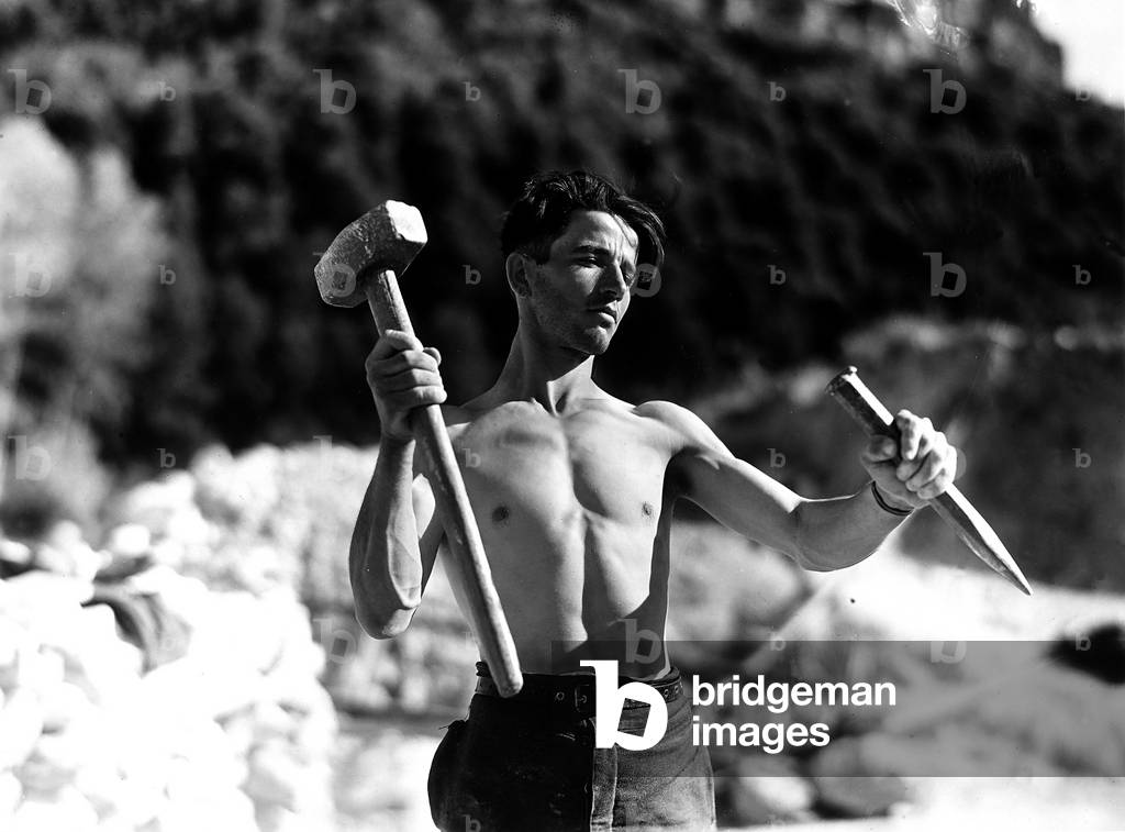 Laconi Cave: Photograph of a bare-chested worker with mallet and a chisel. The photograph was commissioned by the ILVA factory of Genoa. (b/w photo)