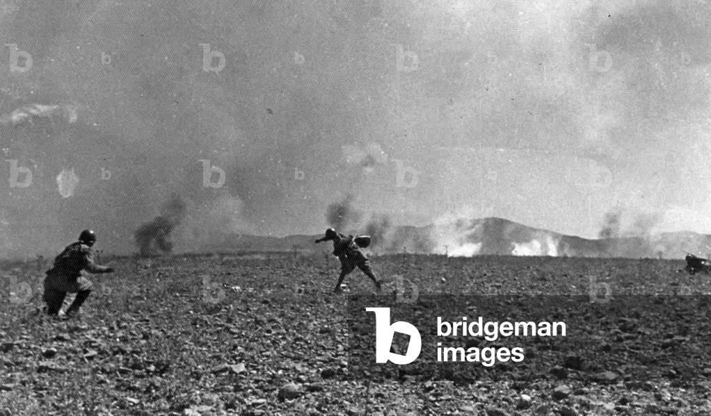 Two soldiers photographed on July 15, 1938, during drill for throwing incendiary bombs. The two soldiers have just finished launching their bombs and the smoke from various explosions can be seen in the distance (b/w photo)
