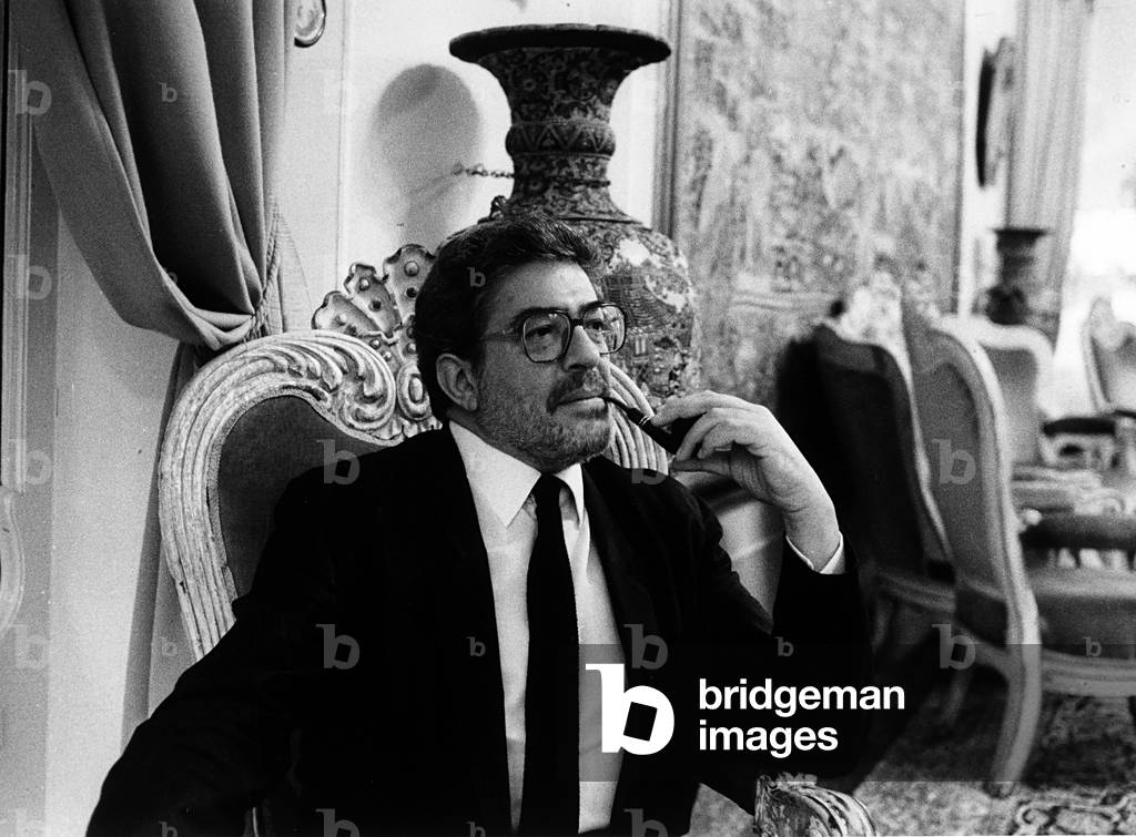 Portrait of the director Ettore Scola, sitting indoors while smoking a pipe.