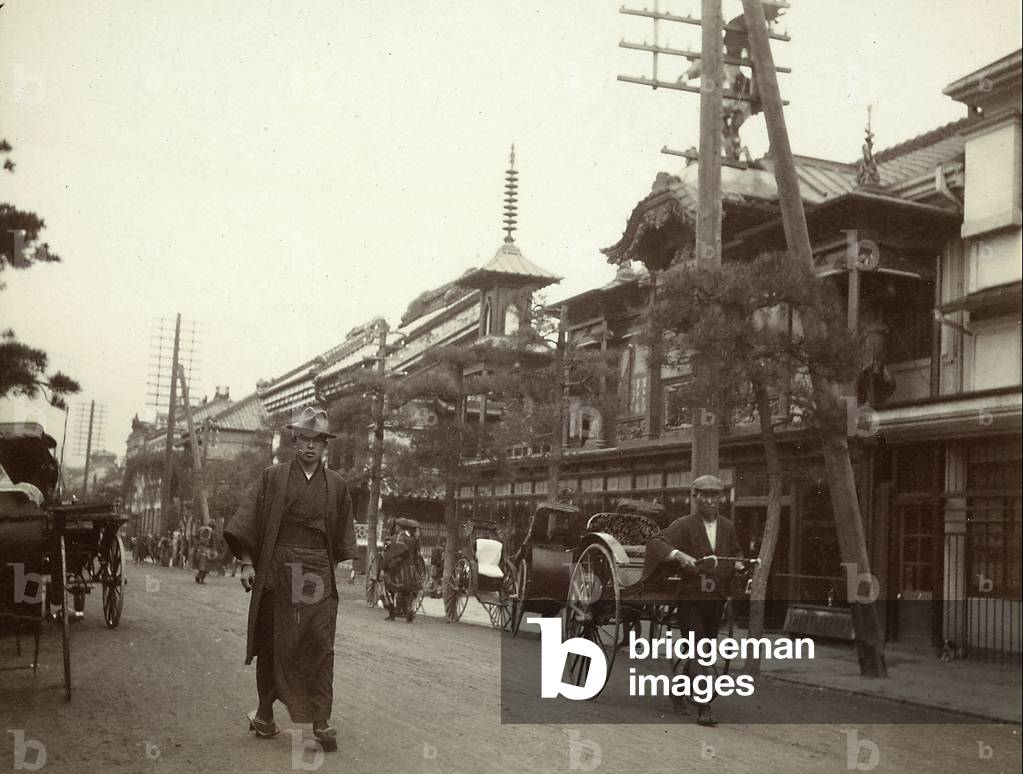 A young japanese man wearing his traditional clothes and a rickshaw in the street of a japanese small town,  1920-1930 (print on double-weight paper)