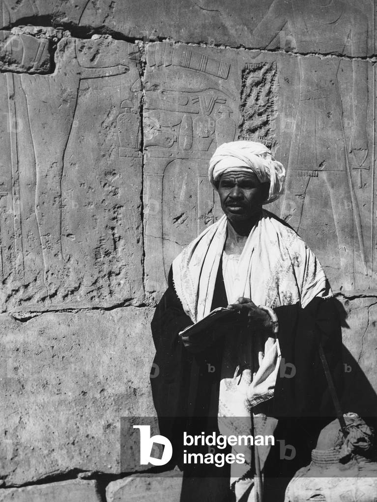 Man portrait near a wall engraved with figures of deities, Egypt