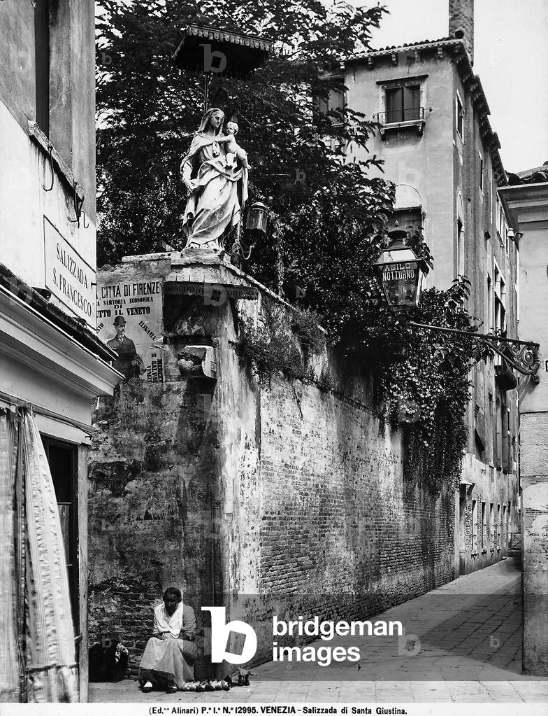 View of the Salizzada di Santa Giustina in Venice. On the left, under a copper canopy, the sculptural group depicting the Madonna and Child, by Giuseppe Torretti, can be seen.