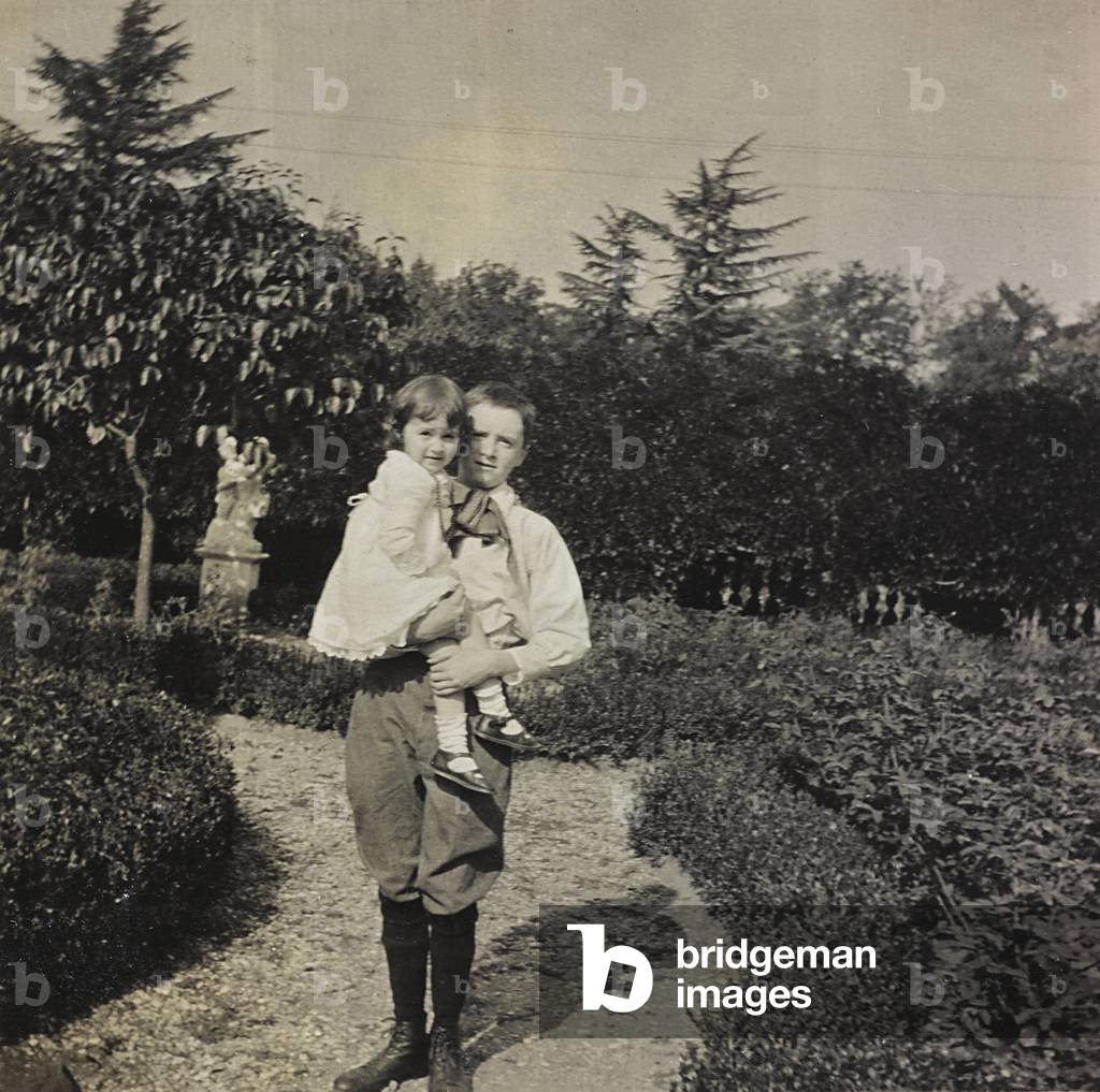 Portrait of a boy with a little girl in her arms in a garden; the support contains the indication 
