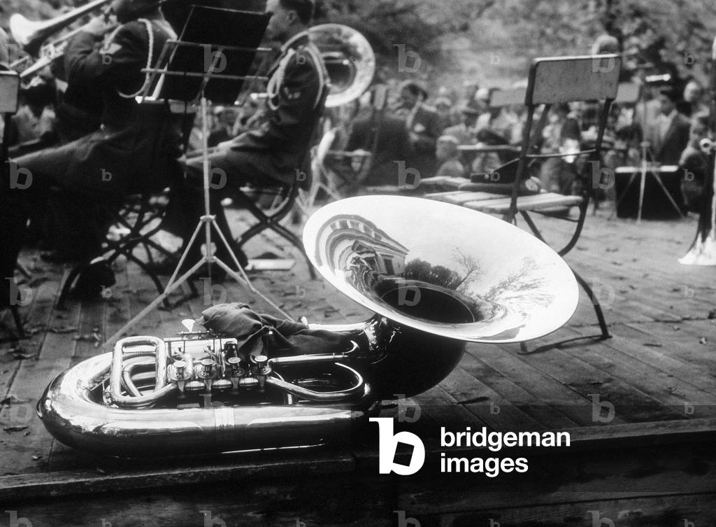 A bass tuba. In the background, a few of the memeber of a military band, during a concert
