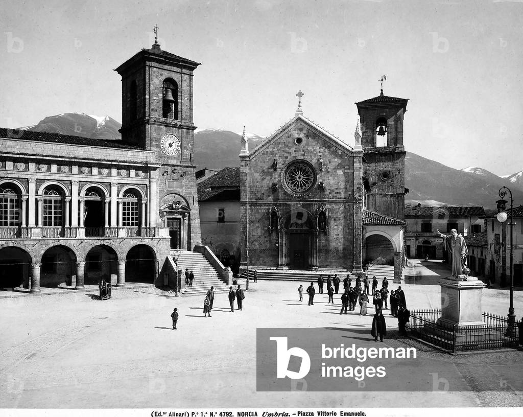 View of Piazza S. Benedetto in Norcia with the City Hall, the Church of St. Benedict and the Monument of St. Benedict. The square is crowded with numerous passers-by.
