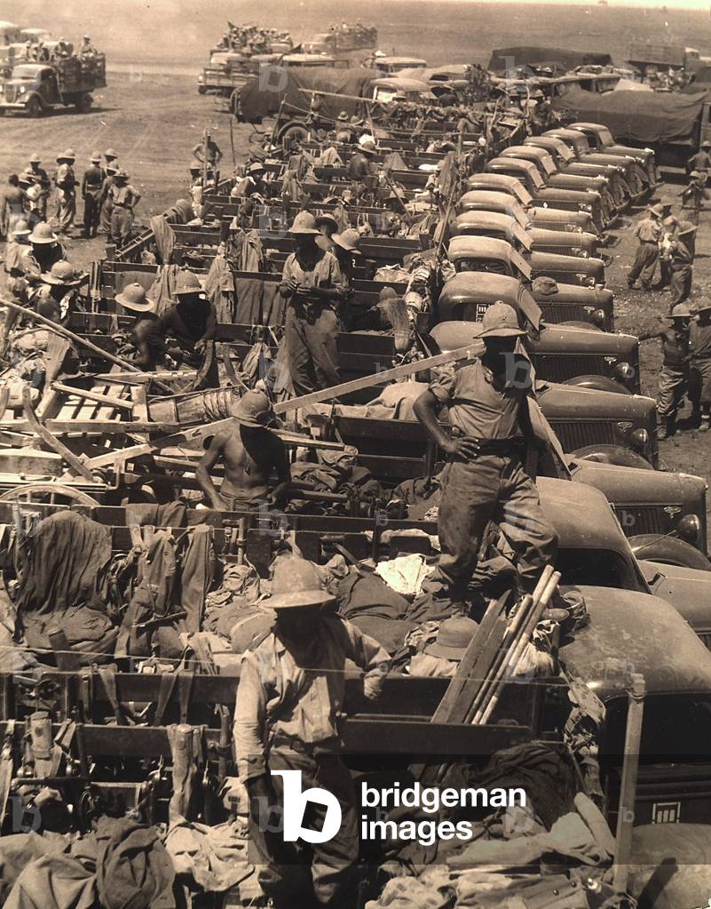 A row of military vehicles with heavy cargo and soldiers on a street in East Africa (b/w photo)